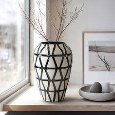 a black and white vase sitting on top of a wooden table next to a window