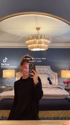 a woman is taking a selfie in front of a bed with chandelier