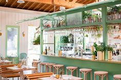 the interior of a restaurant with tables and stools, plants on the bar shelves