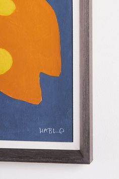 an orange and blue painting hanging on a wall next to a white wall with the word hello written below it