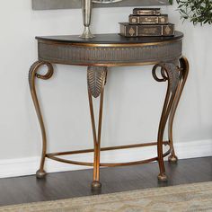 an ornate console table with books on top and a vase sitting on the side, in front of a white wall