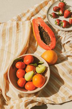 a bowl of fruit sitting on top of a table next to a plate of strawberries