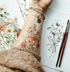 a woman's arm with flowers on it and two pencils next to her