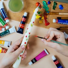 two hands are holding paint sticks and some other crafting supplies next to them on a table