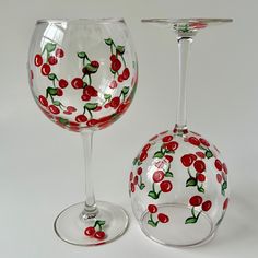 two wine glasses with cherries painted on them sitting next to each other in front of a white background