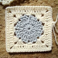 a crocheted square with a blue and white flower on it sitting on the ground