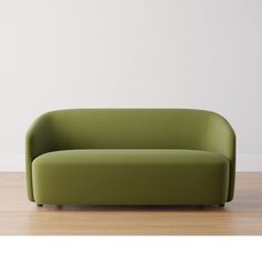 a green couch sitting on top of a hard wood floor next to a white wall