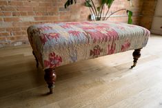 an upholstered bench in front of a brick wall and potted plant on the floor