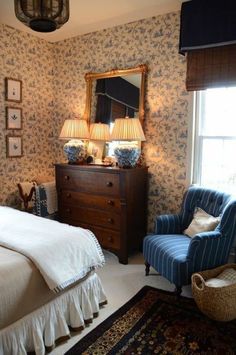 a bed room with a neatly made bed next to a dresser and a chair in front of a window