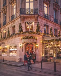 two people are standing in front of a building decorated with christmas lights and garlands