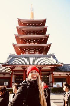 a woman standing in front of a tall building with a red hat on her head