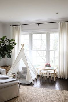 a white teepee tent sitting on top of a wooden floor next to a window