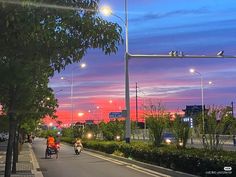 people are riding bikes down the street at sunset or dawn with traffic lights in the background