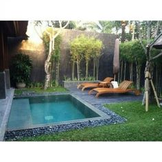 a small pool in the middle of a yard with lounge chairs and trees around it