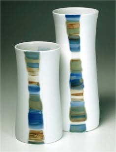 two white vases sitting next to each other on a gray surface with blue and green designs