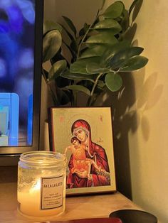 a candle sitting on top of a wooden table next to a painting and a potted plant