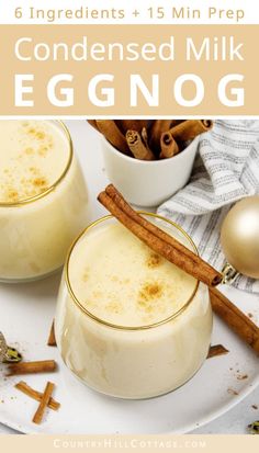 two glasses filled with eggnog on top of a white plate next to cinnamon sticks