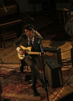 a man in a suit and tie playing an electric guitar while singing into a microphone