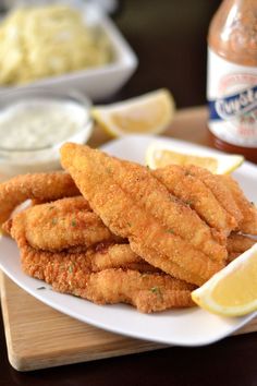 fried fish sticks on a white plate with lemon wedges next to dip and cole slaw