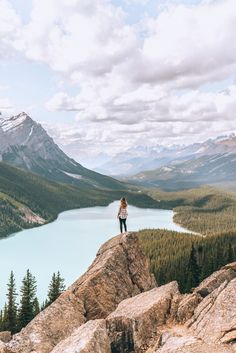 a person standing on top of a large rock next to a body of water with mountains in the background