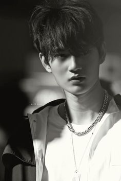 black and white photo of a young man with short hair wearing a jacket, necklace and shirt