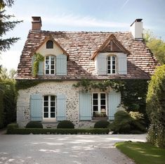 an old house with blue shutters and stone walls, surrounded by greenery on both sides