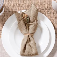 a white plate topped with a napkin wrapped in burlock next to a vase