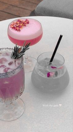 two cocktails sitting on top of a table next to each other, one with a pink drink in it