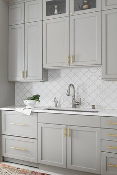 a kitchen with gray cabinets and white counter tops, gold handles on the faucet