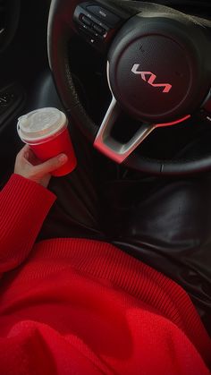 a person holding a cup in their hand while sitting in the driver's seat