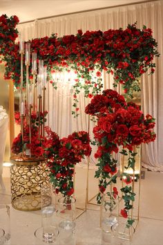 red roses and greenery are arranged in tall glass vases on a white table