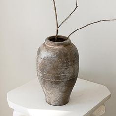 a vase sitting on top of a white table with a twig sticking out of it