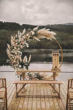 an outdoor ceremony setup with flowers and pamodia on the table, along with two wooden chairs