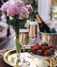 two champagne flutes and strawberries on a gold platter with pink flowers in the background