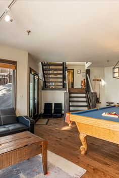 a pool table in the middle of a living room with stairs leading up to the second floor