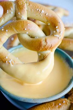 pretzel rings being dipped with mustard in a blue bowl next to other pretzels