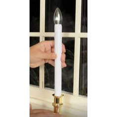 a person holding a white candle in front of a window with the light on it