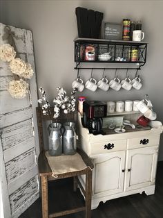 a coffee bar with cups and mugs on the top shelf, next to an old door