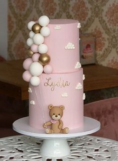 a pink cake with white and gold balloons on the top is decorated with a teddy bear