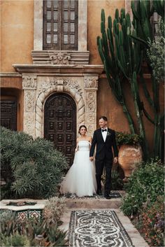 a bride and groom are standing in front of an old building with cactuses on the ground