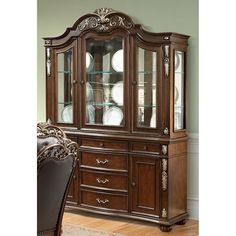 a wooden china cabinet with glass doors and ornate carvings on the front, along with a brown leather chair