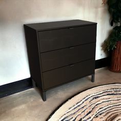 a black dresser sitting next to a potted plant on top of a carpeted floor