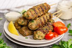 there are several skewers of meat on the plate with tomatoes and parsley