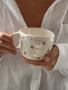 a woman is holding a cup with writing on it and has her hands in the cup