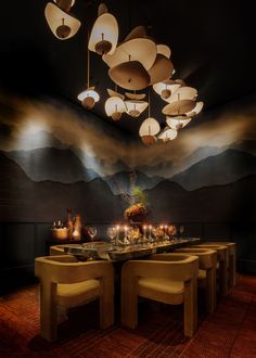 a dining room table and chairs with lights hanging from the ceiling above it in front of a mountain backdrop