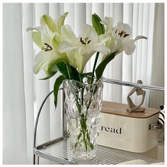 some white flowers are in a clear vase on a metal shelf next to a box