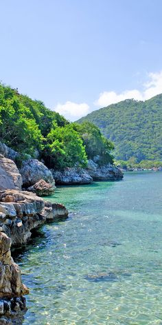 the water is crystal blue and clear with green trees in the background, along with rocks on both sides