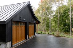 a black garage with two brown doors in front of trees