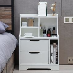 a bedroom with a bed, nightstand and shelf next to it on the floor in front of a gray wall