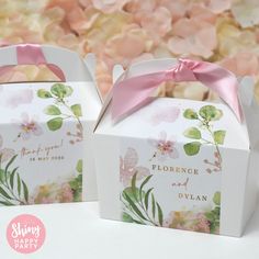 two white boxes with pink bows on them sitting next to each other in front of flowers